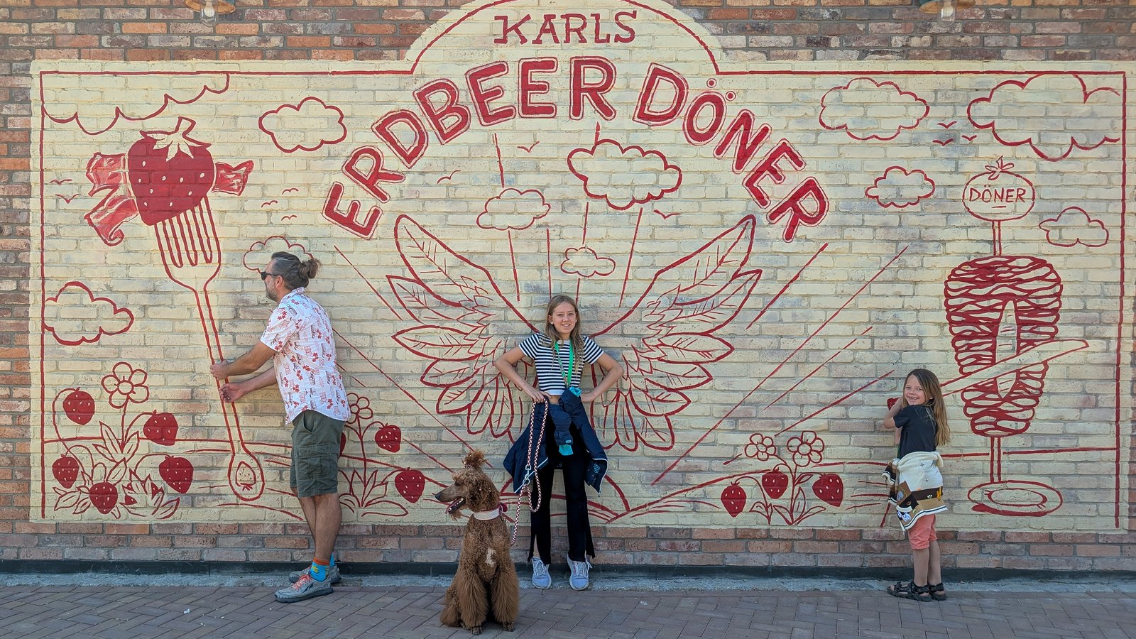Familie mit Hund vor der gemalten Erdbeer-Döner-Wand bei Karls in Elstal