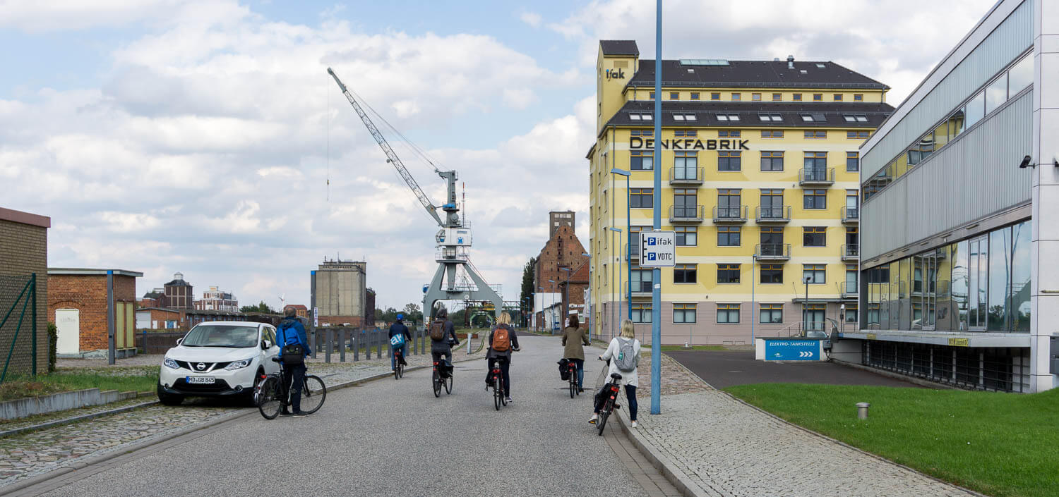 Radfahrer auf der Hafenstraße im Wissenschaftshafen Magdeburg, dahinter ein alter Hafenkran und das gelbe Gebäude Denkfabrik