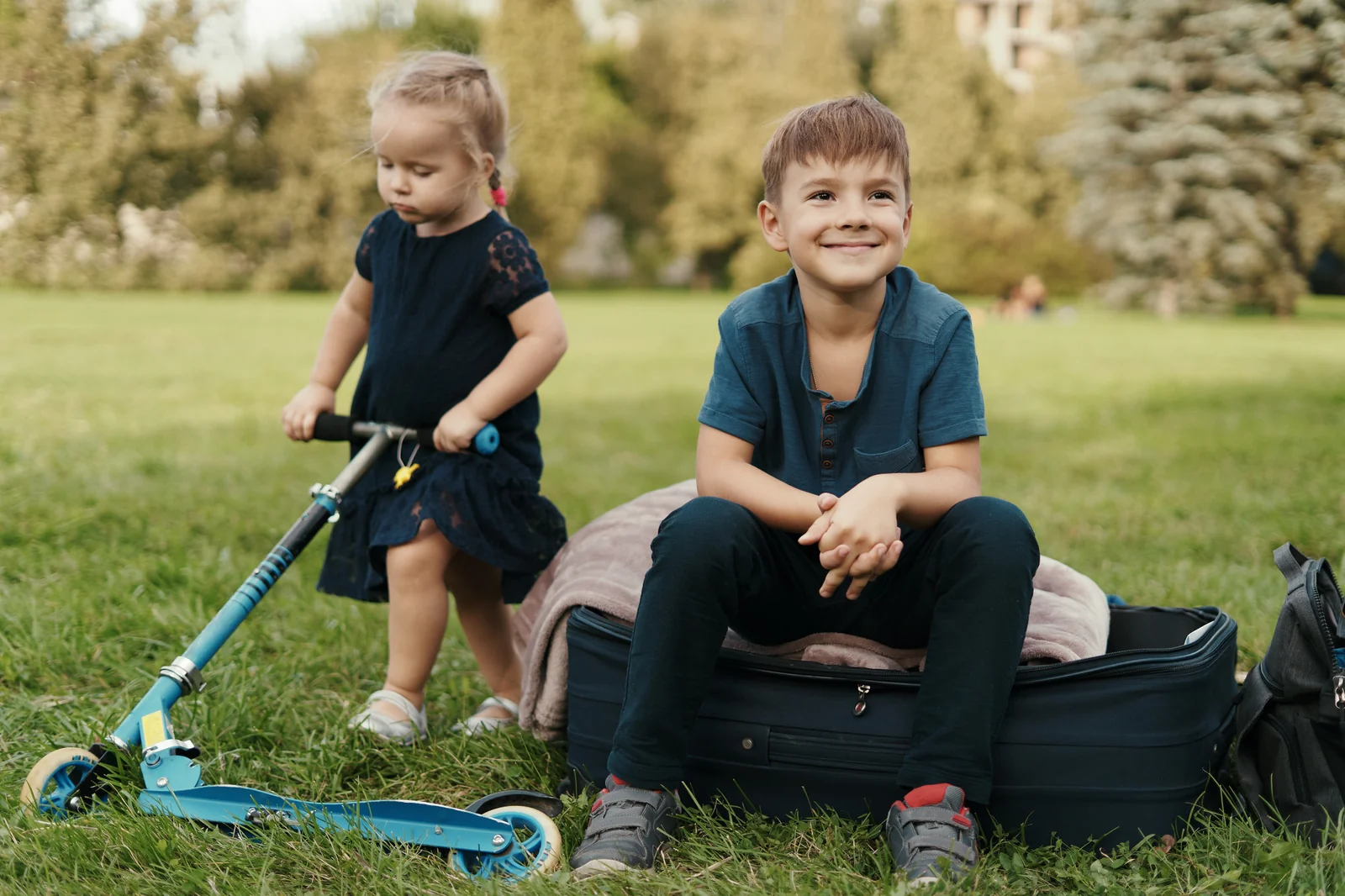 Ein kleines Mädchen mit Scooter und ein lächelnder Junge auf einer Wiese im Park.